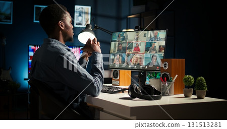Black guy meeting with group of individuals on web video conference, uses technology for virtual communication. Freelancer working remotely, online meetings or classes in a cozy home. Camera A. Black guy meeting with group of individuals on web video conference, uses technology for virtual communication. Freelancer working remotely, online meetings or classes in a cozy home. Camera A. 131513281