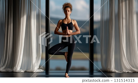 Woman in tree pose with hands in anjali mudra and eyes closed, practicing mindful yoga in a bright studio by the lake, embodying balance, calm and inner peace 131514315