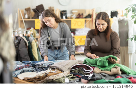 During November sales, Latin woman choose something warm clothes, other client in background 131514940