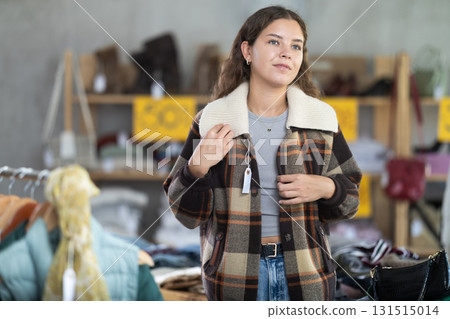During November sales, young woman choose and try on checkered coat-jacket, view reflection in mirror. 131515014