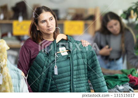 Female shopper chooses winter down coat in clothing store 131515017