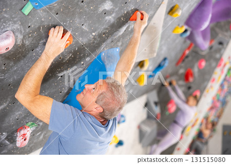 Focused active aged man climbing on bouldering wall Focused active aged man climbing on bouldering wall 131515080