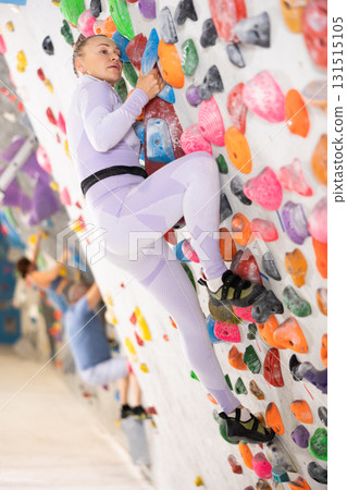 Adult woman practicing rock climbing on climbing wall 131515105