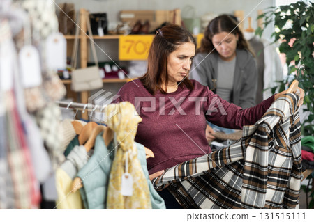 Female shopper chooses beautiful checkered coat-jacket in clothing store Female shopper chooses beautiful checkered coat-jacket in clothing store 131515111