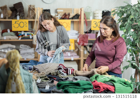 Latina woman carefully selects a warm sweater, pullover or cardigan in clothing store 131515118