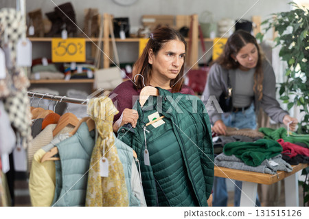 Female shopper chooses winter down coat in clothing store Female shopper chooses winter down coat in clothing store 131515126