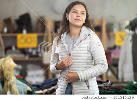 Positive young woman trying on white down jacket in clothing store Positive young woman trying on white down jacket in clothing store 131515129