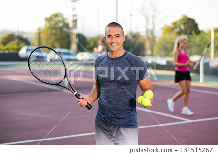 Positive sportsman looking at camera while playing tennis at court outdoor Positive sportsman looking at camera while playing tennis at court outdoor 131515267