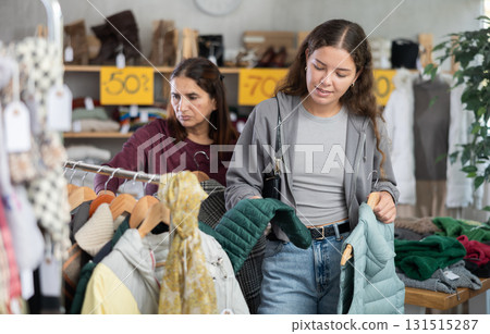 Young girl choosing light green vest for autumn-winter in clothing store Young girl choosing light green vest for autumn-winter in clothing store 131515287