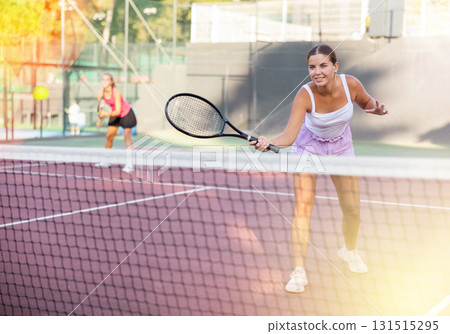 Female player playing tennis in tennis court outdoor behind net 131515295
