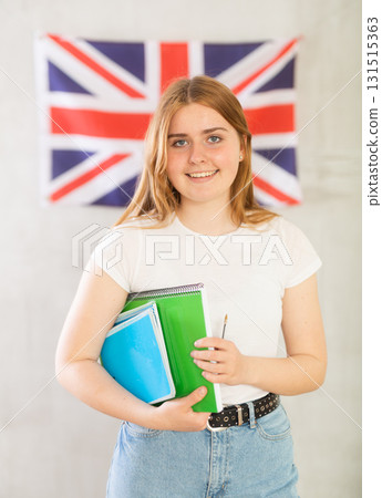 Female student with notebooks stands against wall under flag of Great Britain. Gray background Female student with notebooks stands against wall under flag of Great Britain. Gray background 131515363