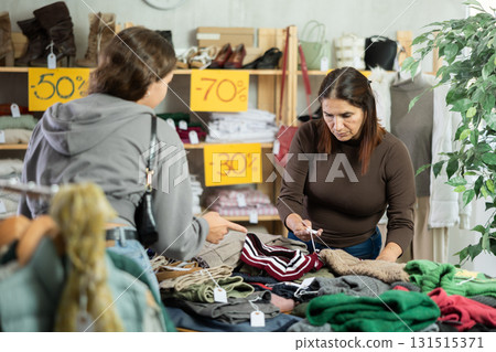 Latina woman carefully selects a warm sweater, pullover or cardigan in clothing store 131515371
