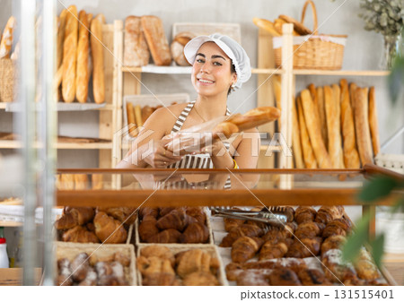 Young saleswoman holds out baguettes in paper bag in bakery Young saleswoman holds out baguettes in paper bag in bakery 131515401