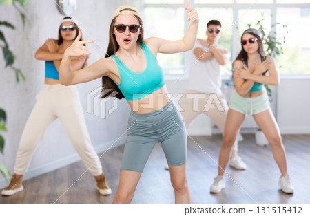 Group of young girls in dark glasses and ball cap and guy dance jazz-funk in fitness club. Group of young girls in dark glasses and ball cap and guy dance jazz-funk in fitness club. 131515412