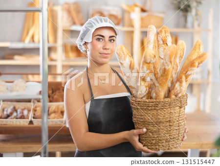 Young saleswoman displays baguettes in wicker basket 131515447