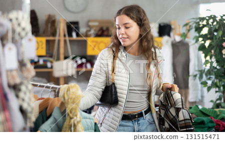 Positive young woman choosing something for autumn-winter in clothing store Positive young woman choosing something for autumn-winter in clothing store 131515471