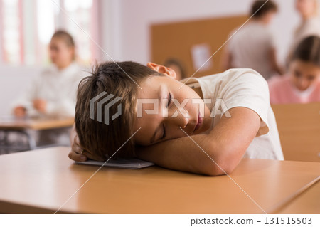 Tired boy sleeping at desk in classroom 131515503