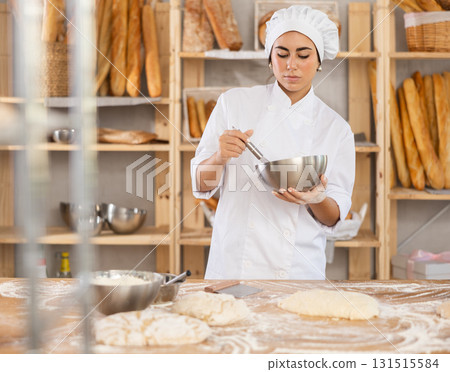 Young female baker whisking dough in bowl 131515584