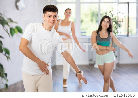 Guy and young girls in good mood actively move and dance reggaeton at choreography lesson Guy and young girls in good mood actively move and dance reggaeton at choreography lesson 131515599
