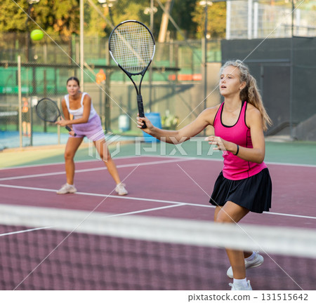 Sporty teenager girl player hitting ball with racket during friendly doubles couple match 131515642