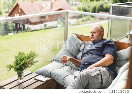 Middle-aged man relaxing on balcony with glass of wine. 131515950