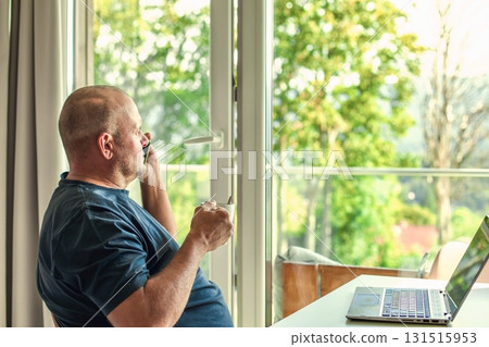 Middle-aged man with laptop, drinking coffee, talking on phone, enjoying window view. Middle-aged man with laptop, drinking coffee, talking on phone, enjoying window view. 131515953