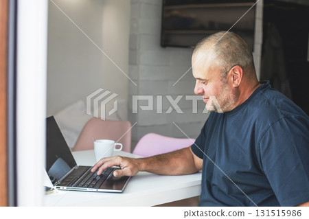 Man working on laptop at home with coffee by the window. Man working on laptop at home with coffee by the window. 131515986