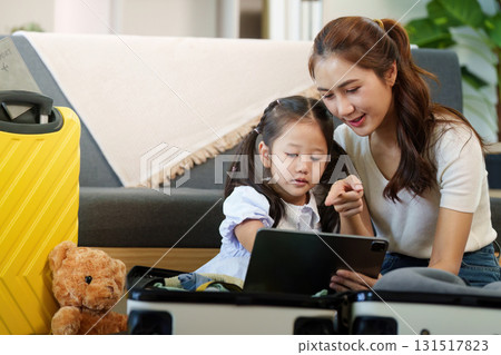 Travel Planning. Mother and daughter engaging with a tablet while packing. 131517823