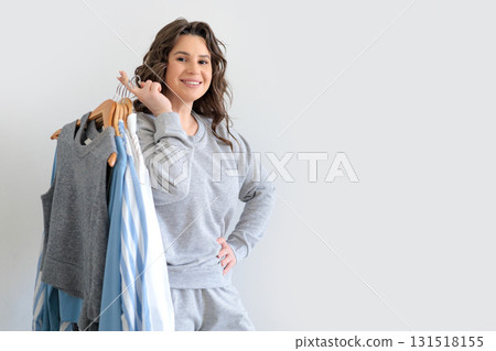 Beautiful European woman in gray knitted suit holds wooden hangers with women's clothes. Beautiful European woman in gray knitted suit holds wooden hangers with women's clothes. 131518155