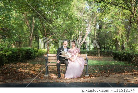 Couple in pink dresses taking wedding photos sitting on a bench in the forest 131518174