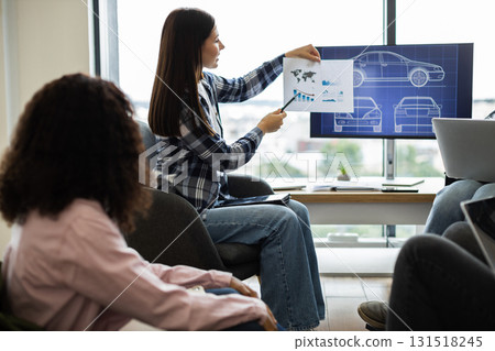Business meeting with young adults presenting car designs and performance analysis using charts. Discussing product development, focusing on automotive concepts Business meeting with young adults presenting car designs and performance analysis using charts. Discussing product development, focusing on automotive concepts 131518245