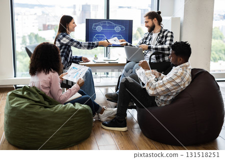 Group of young adults collaborating on vehicle design tasks in open office. Various ethnicities and genders working together, focusing on creativity and teamwork. 131518251