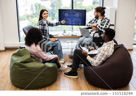 Diverse group of young adults brainstorming car design. Includes man using wheelchair, women, men, different races and teamwork collaboration in open office with plans displayed on screen. Diverse group of young adults brainstorming car design. Includes man using wheelchair, women, men, different races and teamwork collaboration in open office with plans displayed on screen. 131518294