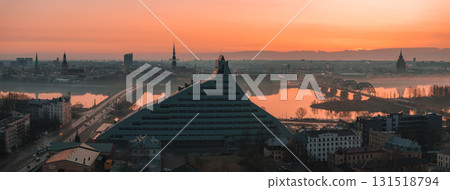 Morning view of Riga, Latvia, featuring the National Library, historic church spires, the Daugava River, and the arched railway bridge in soft mist. 131518794