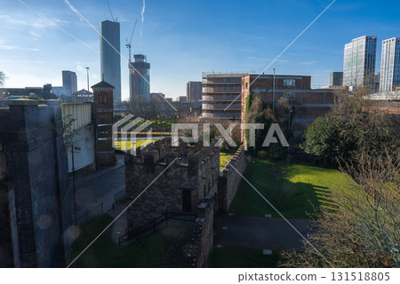 View of Manchester featuring a medieval style stone wall, green spaces, and a skyline with modern skyscrapers and a building under construction. View of Manchester featuring a medieval style stone wall, green spaces, and a skyline with modern skyscrapers and a building under construction. 131518805