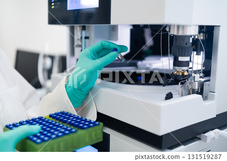 Scientist performing chromatography analysis by inserting vial into automated injection system in laboratory environment. Scientist performing chromatography analysis by inserting vial into automated injection system in laboratory environment. 131519287