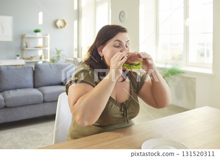 Obese hungry woman with excessive fat eating unhealthy fast food, tasty hamburger, juicy burger 131520311