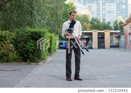 Man assembling telescope tripod and mount in courtyard Man assembling telescope tripod and mount in courtyard 131520442