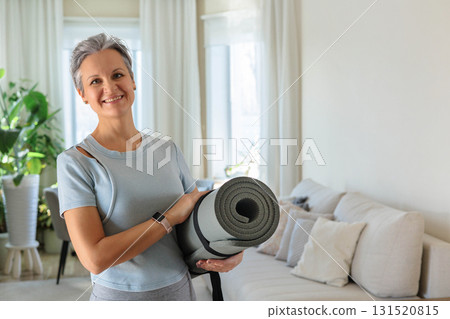 An elderly smiling yogi woman with gray hair is going to practice at home. A mature woman. An elderly smiling yogi woman with gray hair is going to practice at home. A mature woman. 131520815
