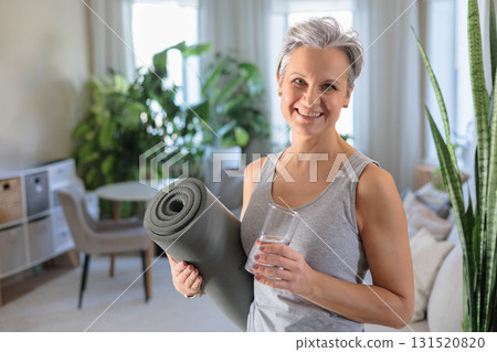 A mature woman of age with gray hair smiles and holds a glass with clean drinking water 131520820