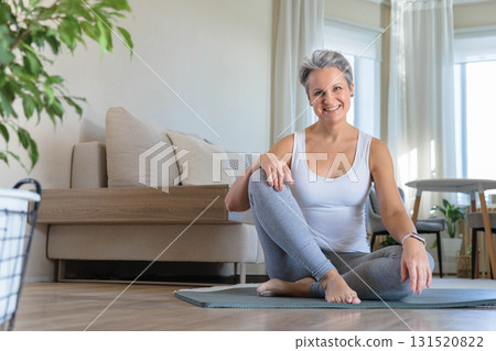 An elderly smiling yogini woman with gray hair sits in the lotus position and meditates at home. An elderly smiling yogini woman with gray hair sits in the lotus position and meditates at home. 131520822