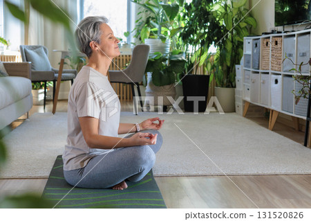 Happy smiling mature middle-aged woman with gray hair does exercises at home and does yoga. 131520826