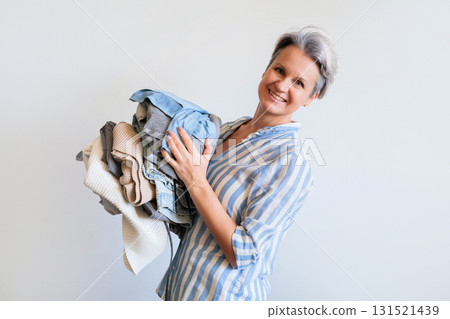 Mature gray haired woman holding stack of clothes isolated on white background 131521439