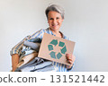 Gray haired woman with pile of clothes and recycling reusing signboard isolated on white background 131521442
