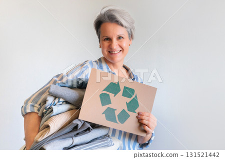 Gray haired woman with pile of clothes and recycling reusing signboard isolated on white background 131521442