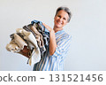 Mature gray haired woman holding stack of clothes isolated on white background 131521456
