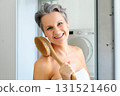 Portrait of smiling gray haired mature woman posing at white bathroom with body clean brush closeup 131521460