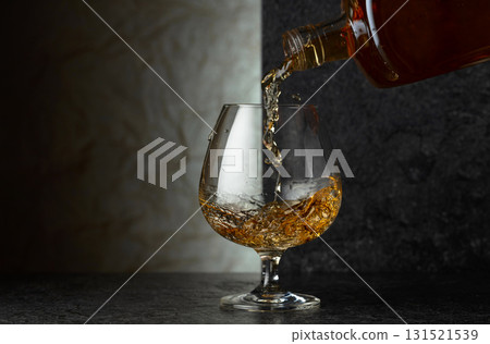Pouring brandy from a bottle into a glass. Pouring brandy from a bottle into a glass. 131521539