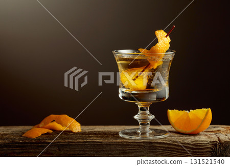 Old Fashioned cocktail in a crystal glass garnished with an orange peel on a old wooden board. Old Fashioned cocktail in a crystal glass garnished with an orange peel on a old wooden board. 131521540