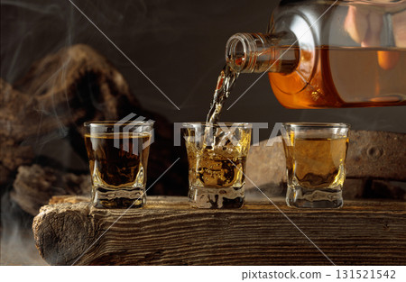 Whiskey is poured from a bottle into a shots. 131521542